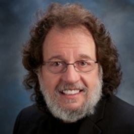 A man with glasses and a beard smiles for the camera