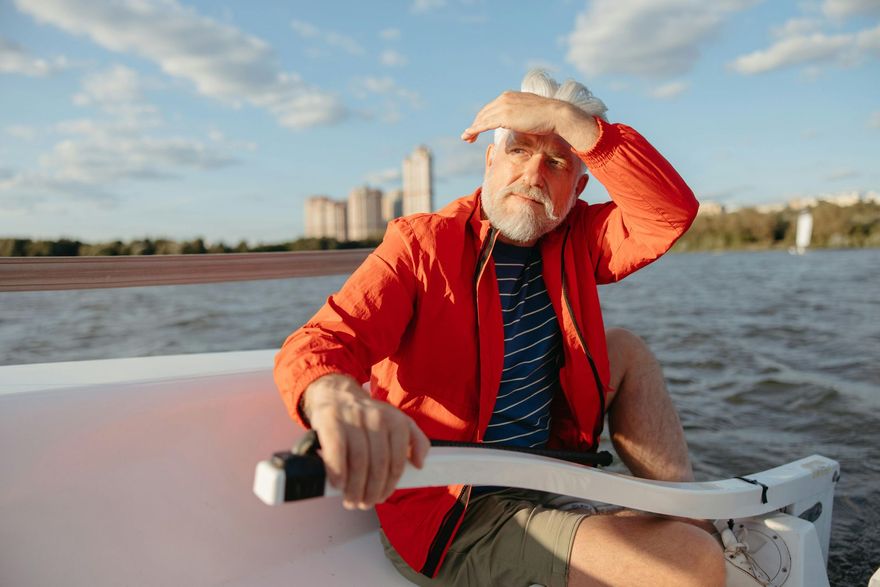 Older man on a boat, shielding his eyes from the sun. He's wearing a red jacket and looking at the water.