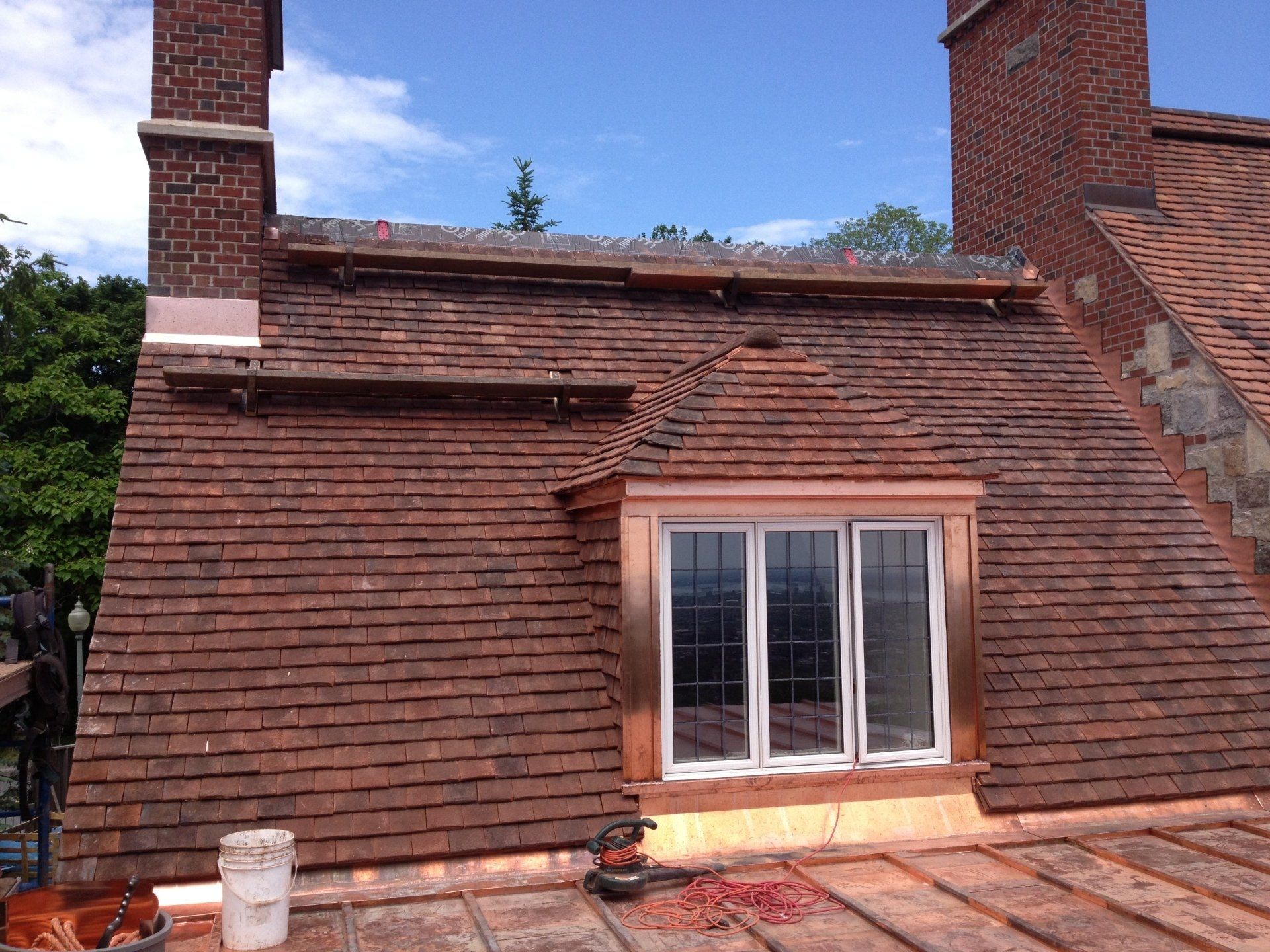 A brick roof with a window and chimney on top of it.