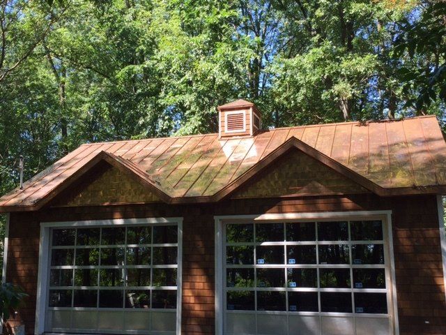 Une maison marron avec un toit en cuivre et deux portes de garage.
