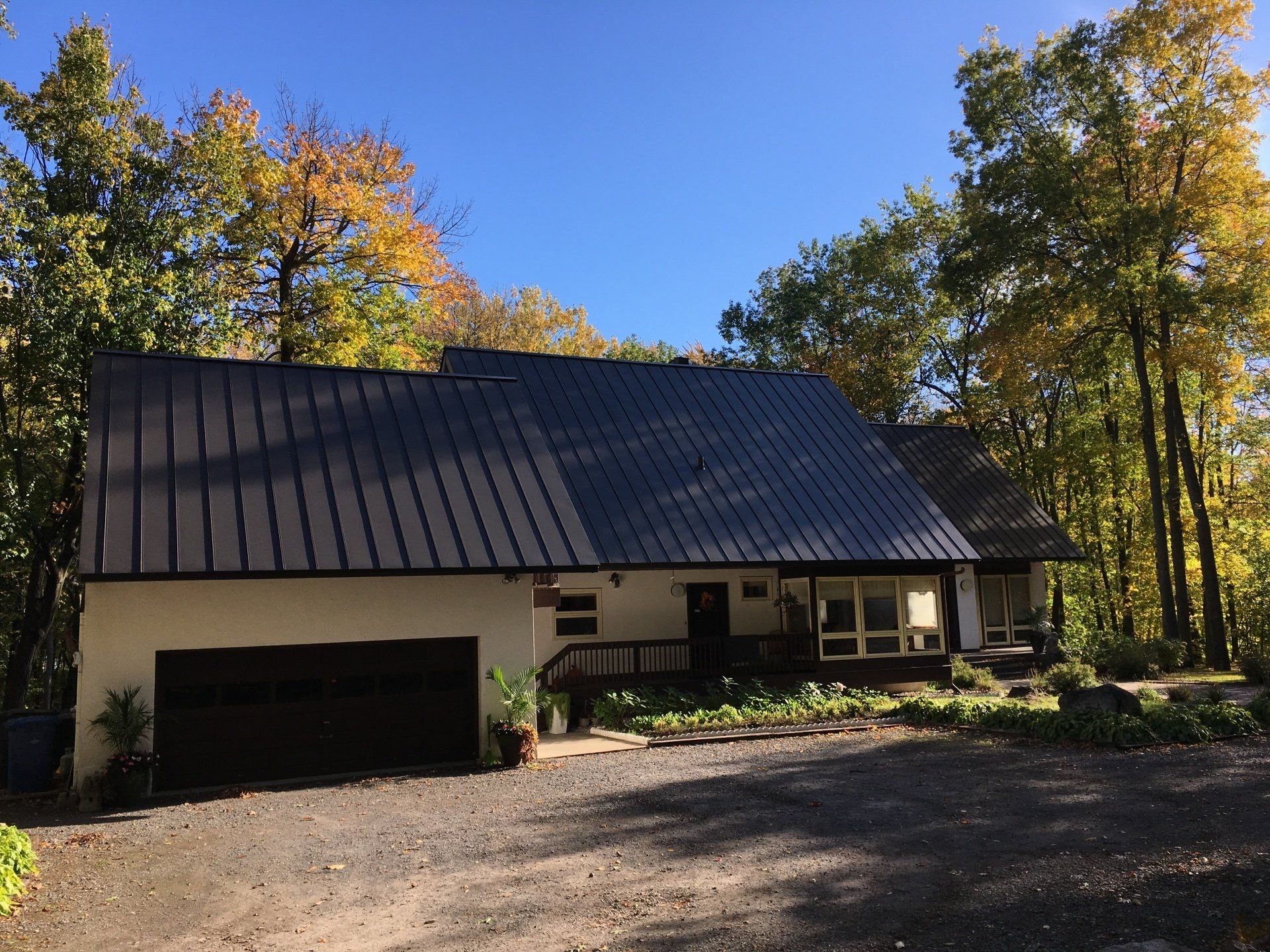 Une maison blanche avec un toit noir est entourée d'arbres