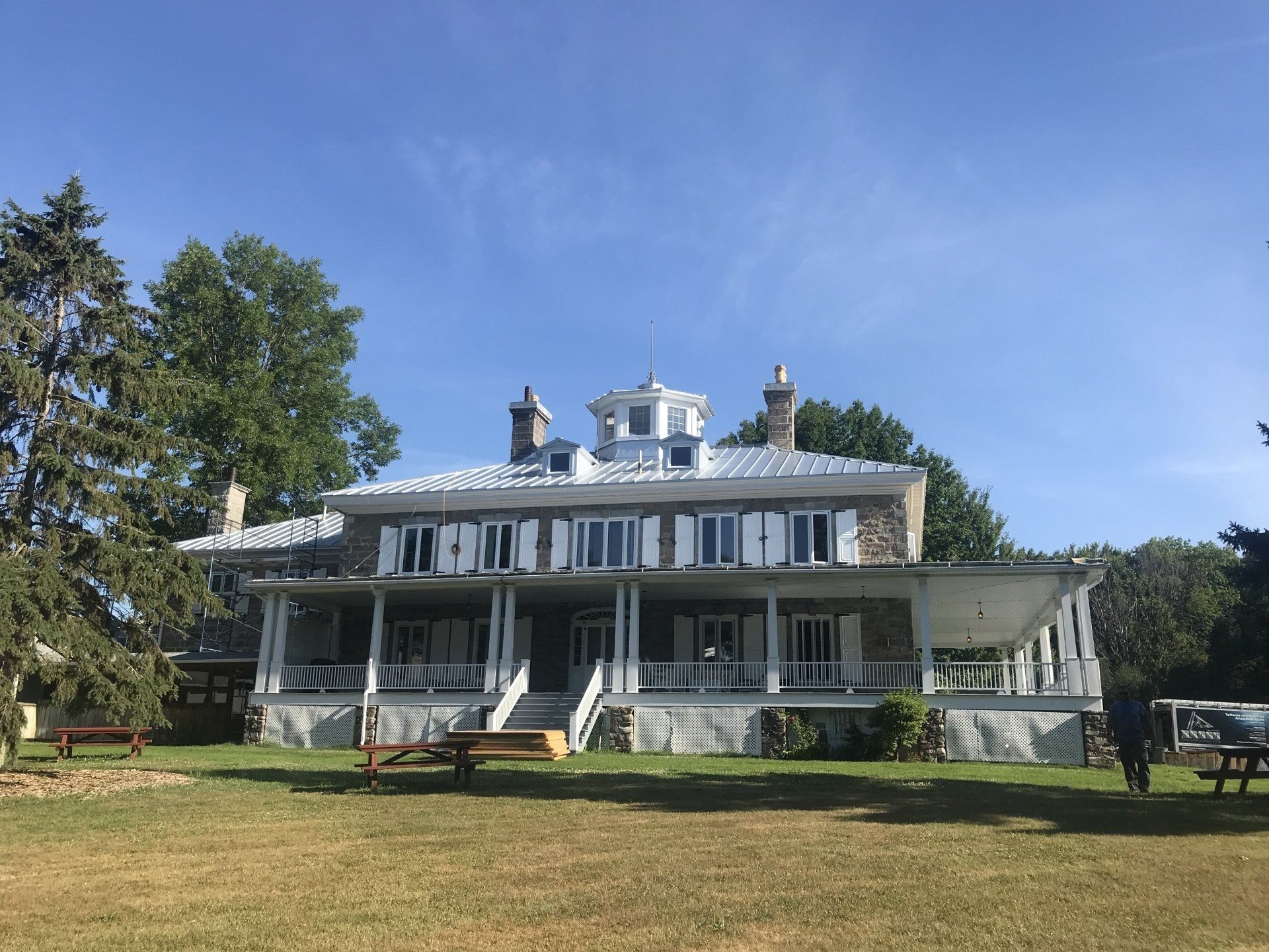 Une grande maison avec un grand porche se trouve au sommet d'un champ verdoyant.