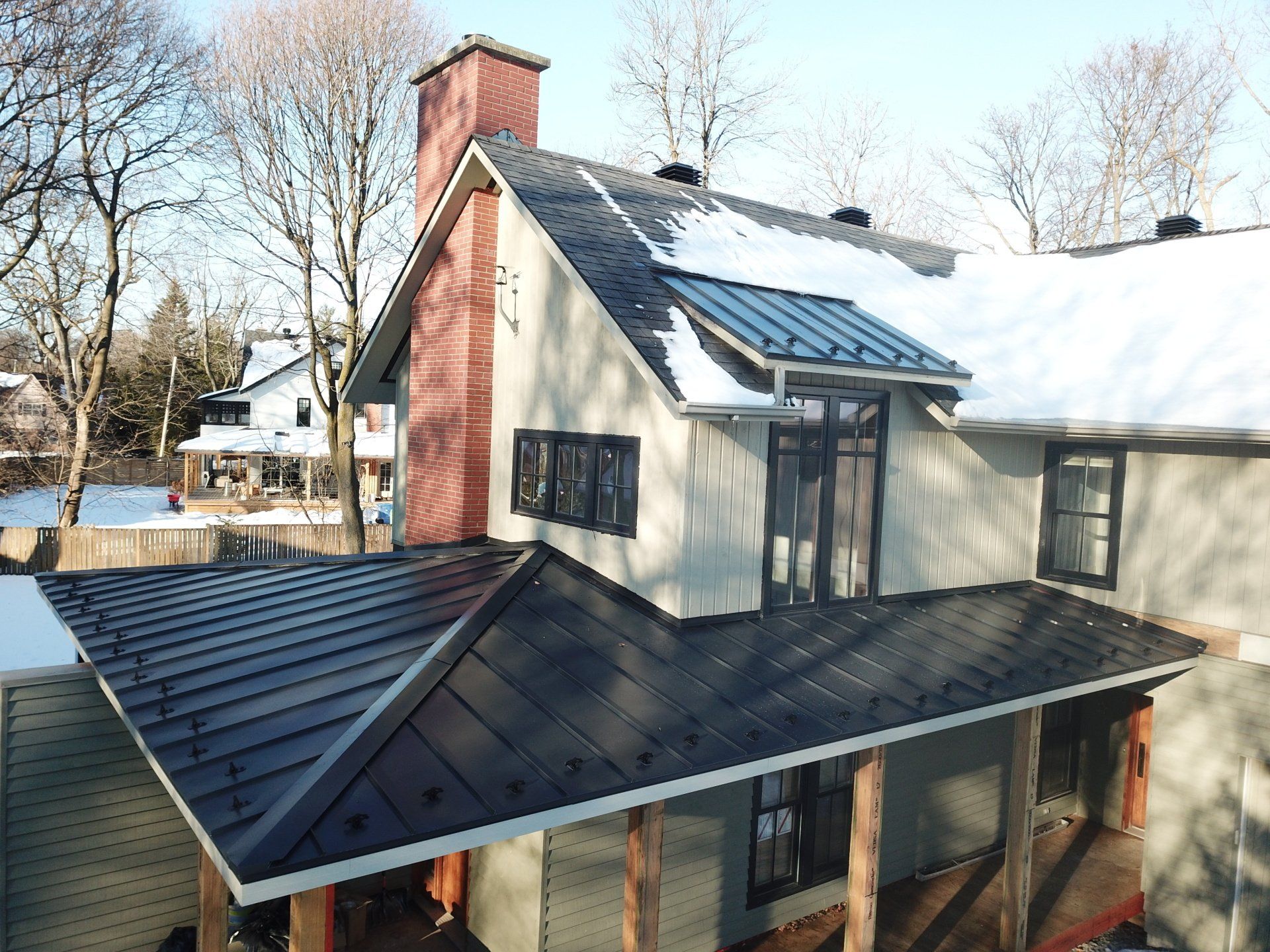 Une vue aérienne d'une maison avec un toit noir et de la neige au sol.