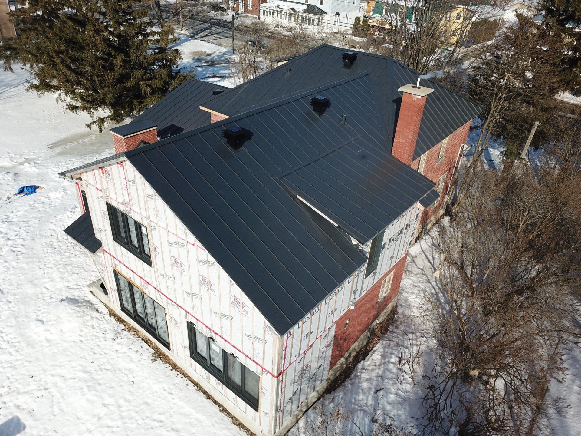 Une vue aérienne d'une maison avec un toit noir dans la neige.