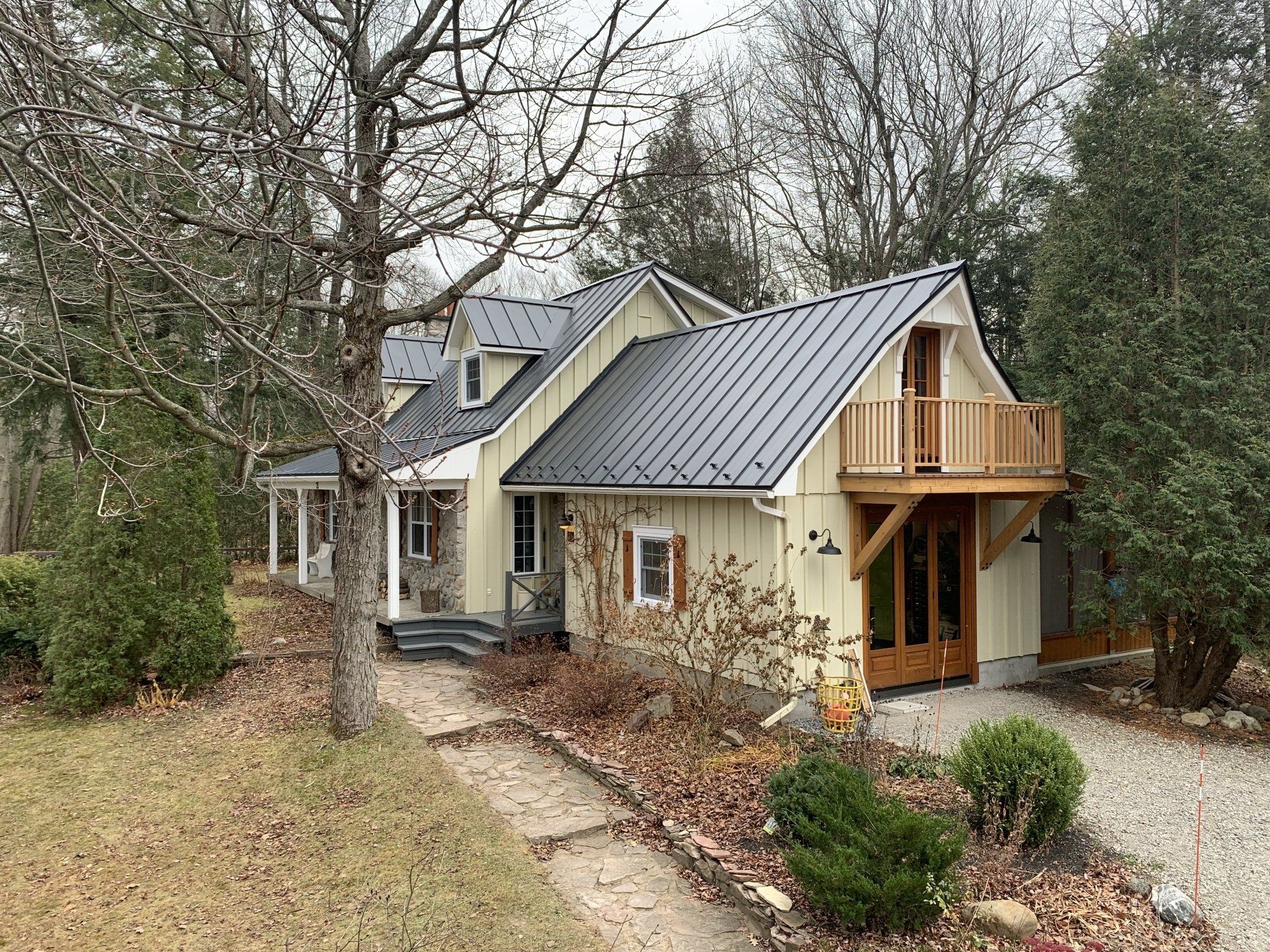 Une maison avec un toit en métal et une terrasse en bois est entourée d'arbres.