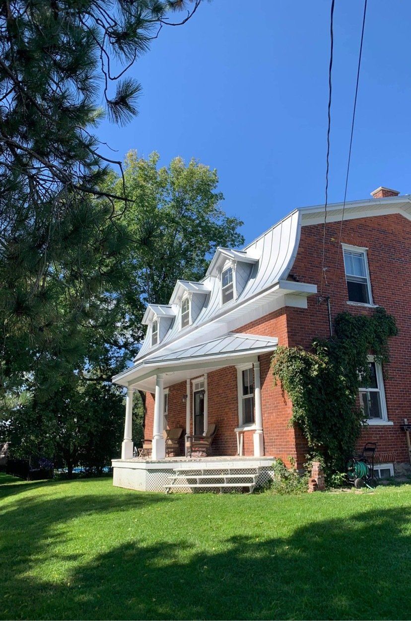 Une maison en brique avec un porche et un toit blanc se trouve au sommet d'une pelouse verdoyante.