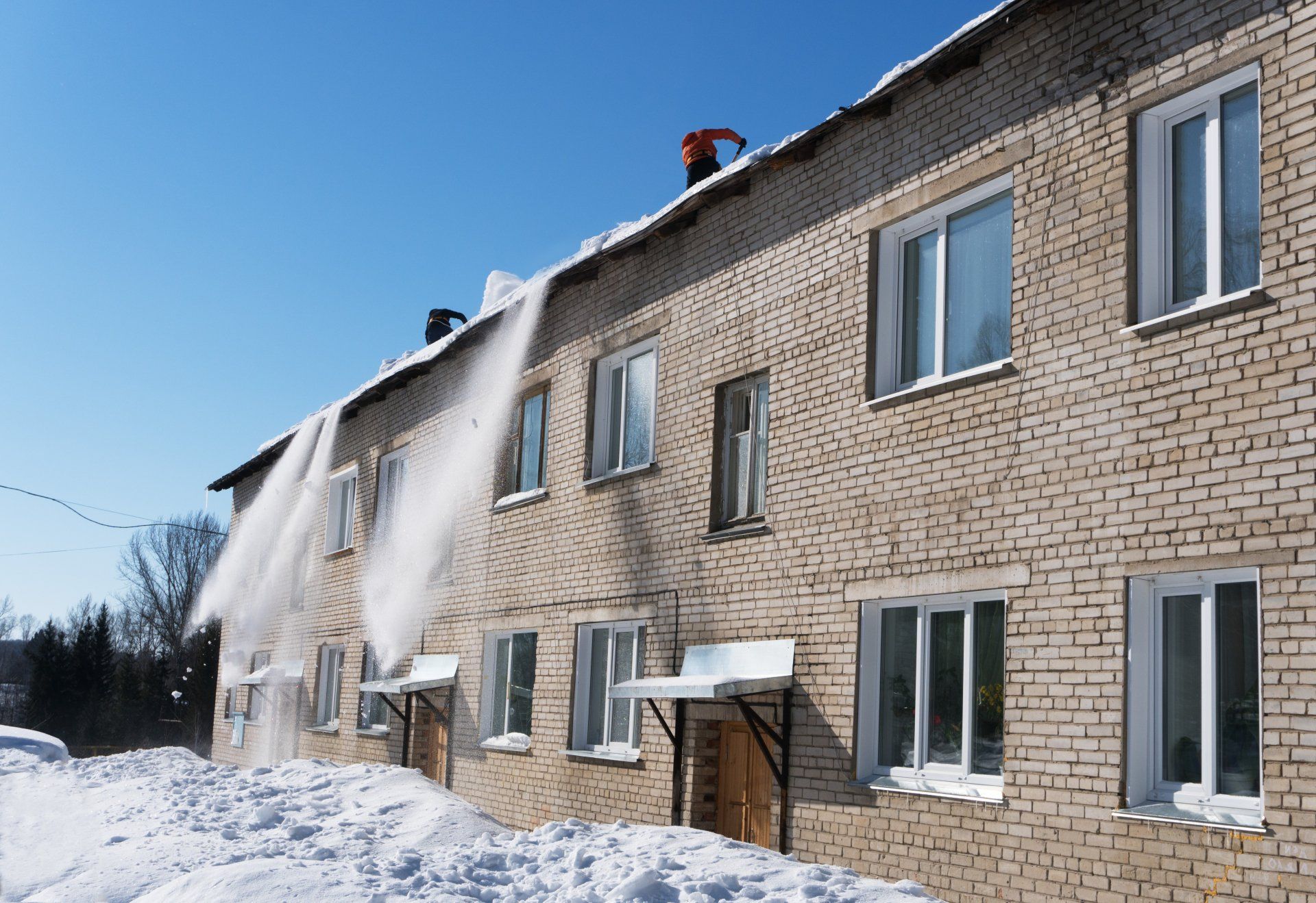 A man is clearing snow from the roof of a brick building