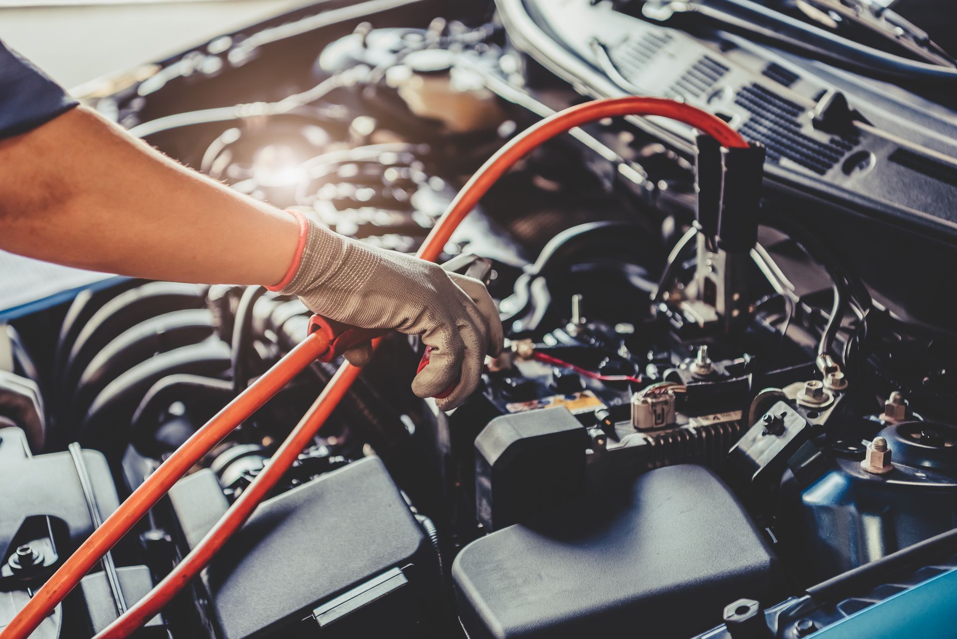 Close-up of a mechanic jump-starting a car battery with red jumper cables.