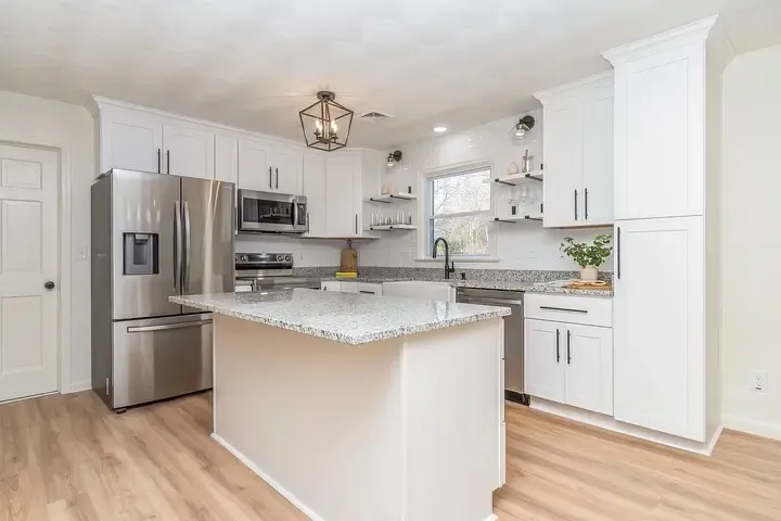 A kitchen with white cabinets , stainless steel appliances , granite counter tops and a large island.