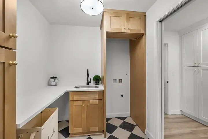 A laundry room with wooden cabinets , a sink , and a checkered floor.