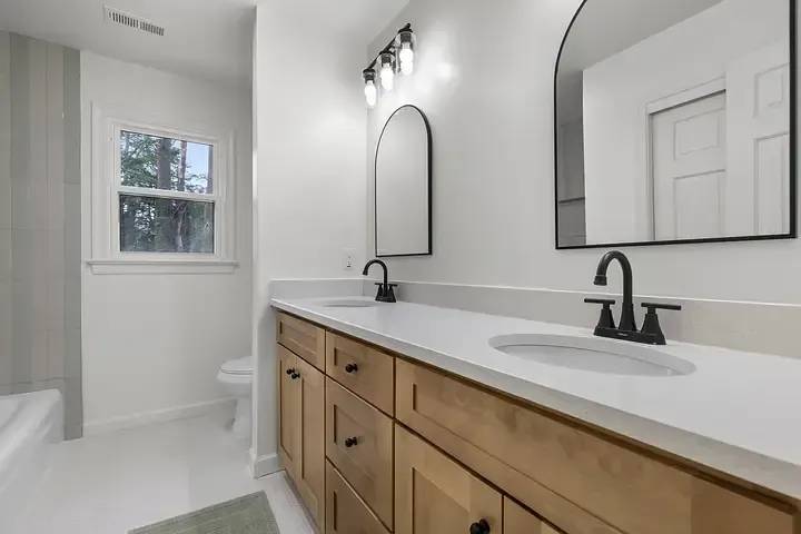 A bathroom with two sinks , two mirrors and a toilet.