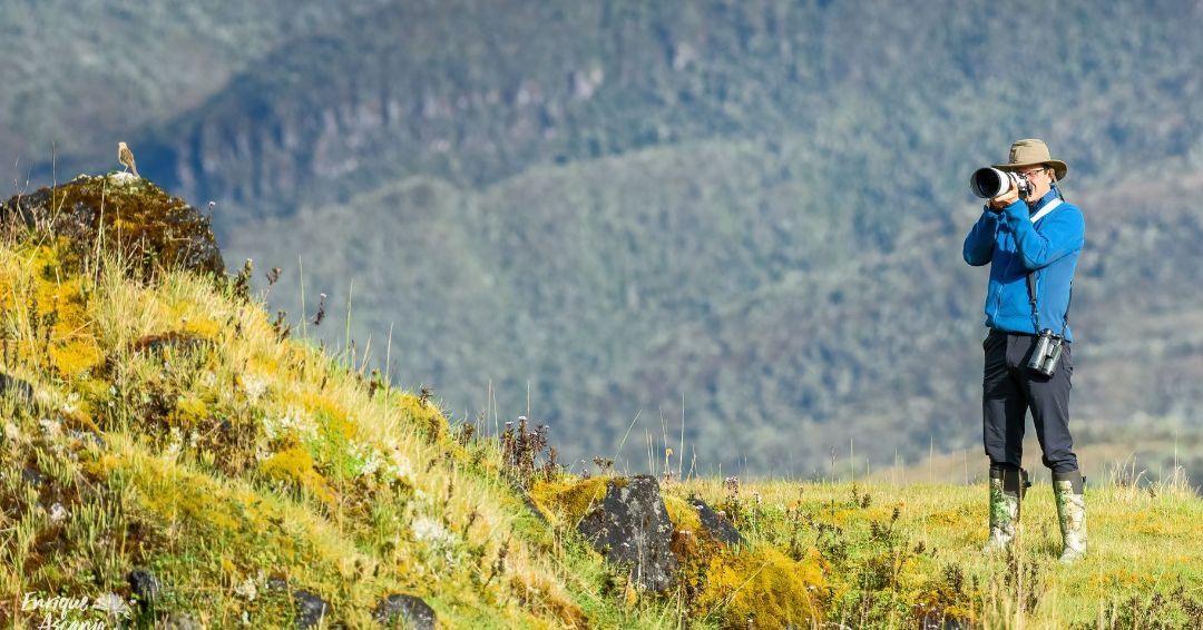 A man is standing on top of a hill taking a picture with a camera.