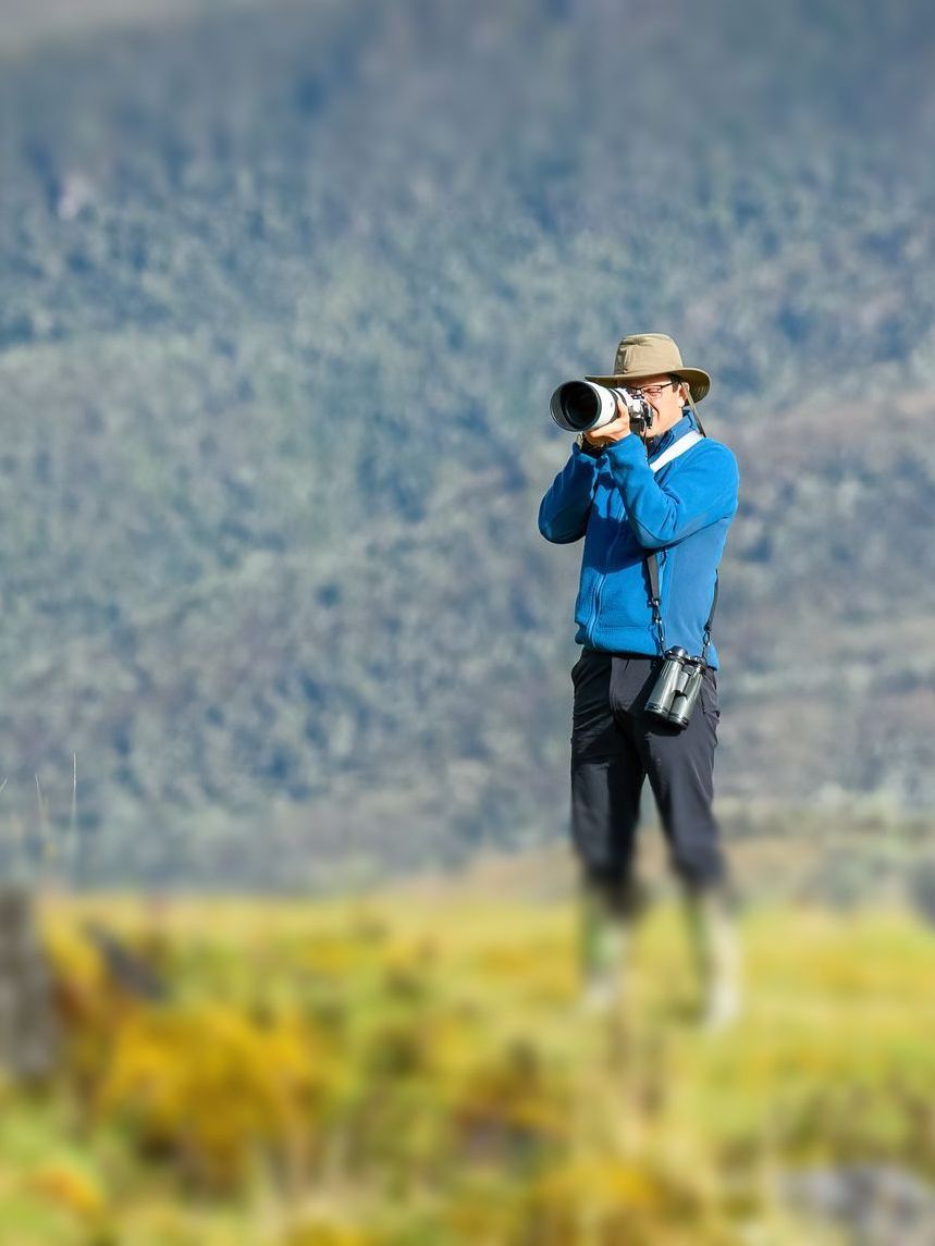 A man is standing in a field taking a picture with a camera.
