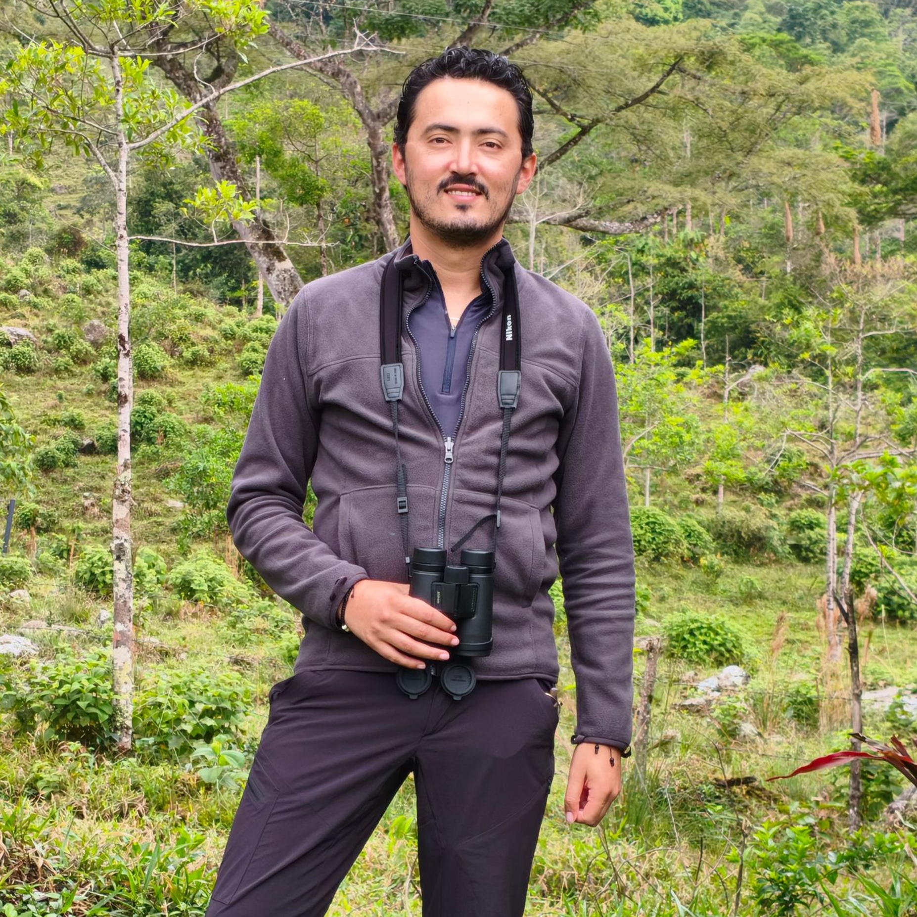 A man wearing suspenders and a light blue shirt is standing in a field.