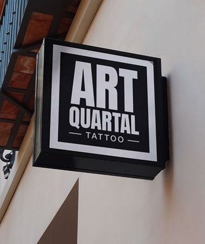 A sign for art quartal tattoo hangs from the side of a building