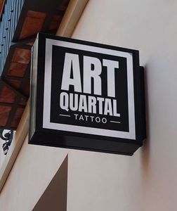 A sign for art quartal tattoo hangs from the side of a building