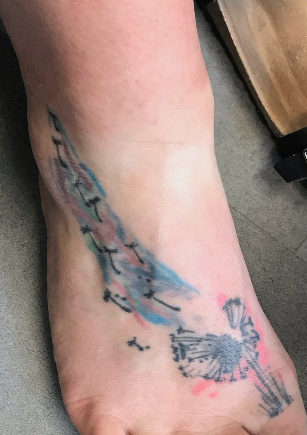 A close up of a person 's foot with a tattoo of a dandelion and feathers