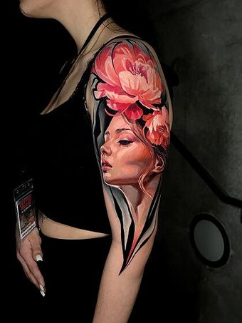 A woman has a tattoo of a woman 's face and flowers on her arm.
