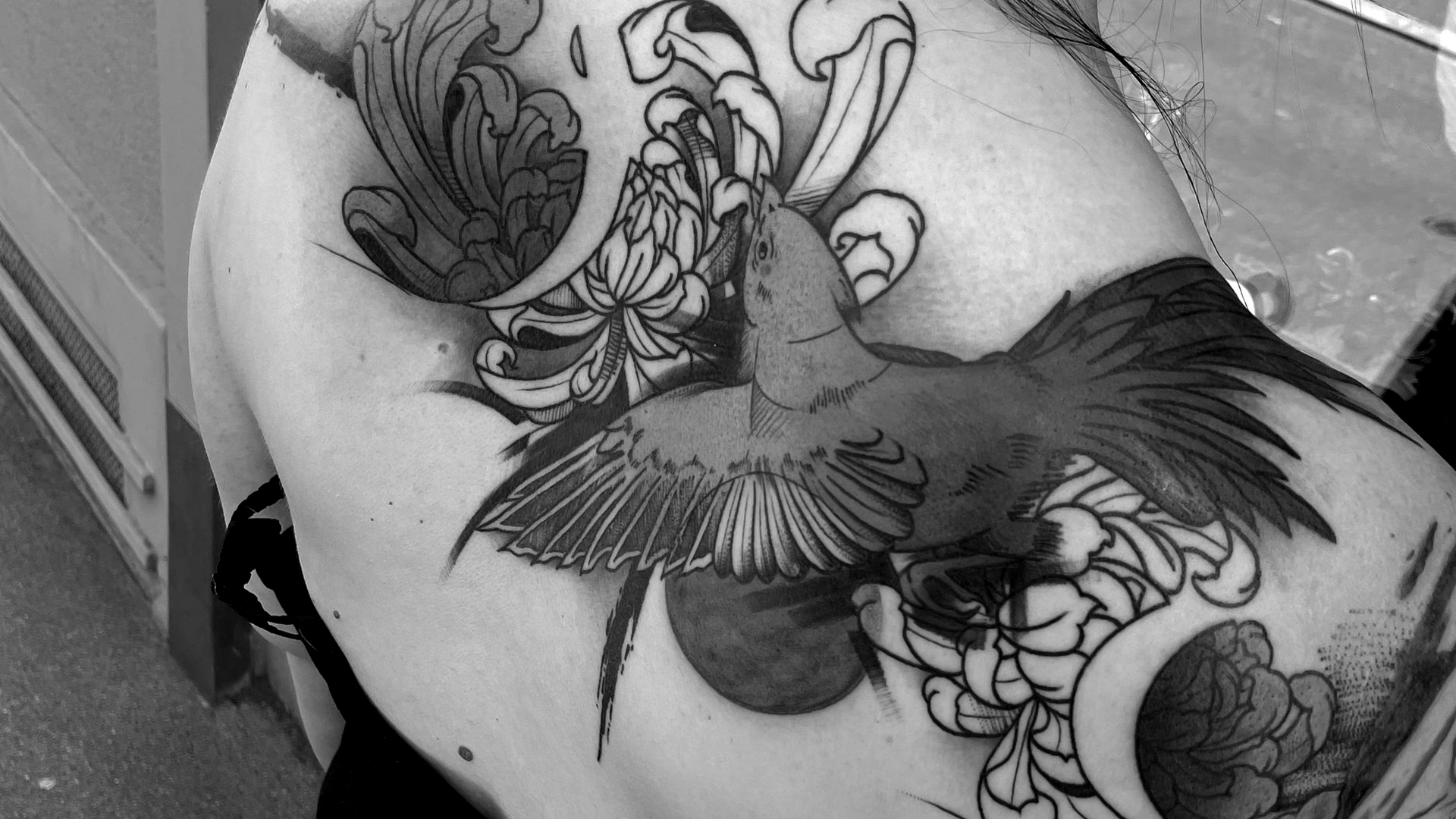 Schwarz-weißes Blumentattoo auf dem Arm einer Person, neben einem Button-Down-Hemd.