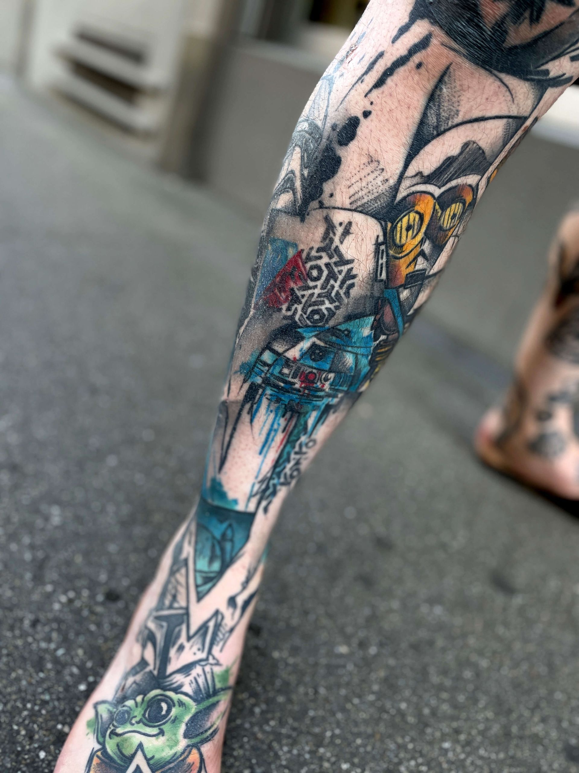 Bein mit farbenfrohen Tattoos mit abstrakten Designs und Figuren vor einer Außenkulisse.