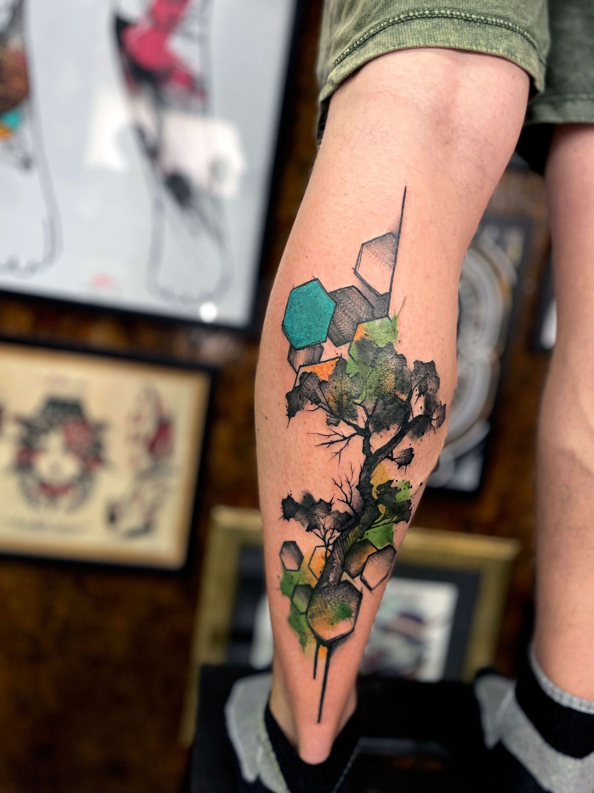 Tätowierung eines Baums auf einem Bein, mit geometrischen Formen und Farbspritzern.