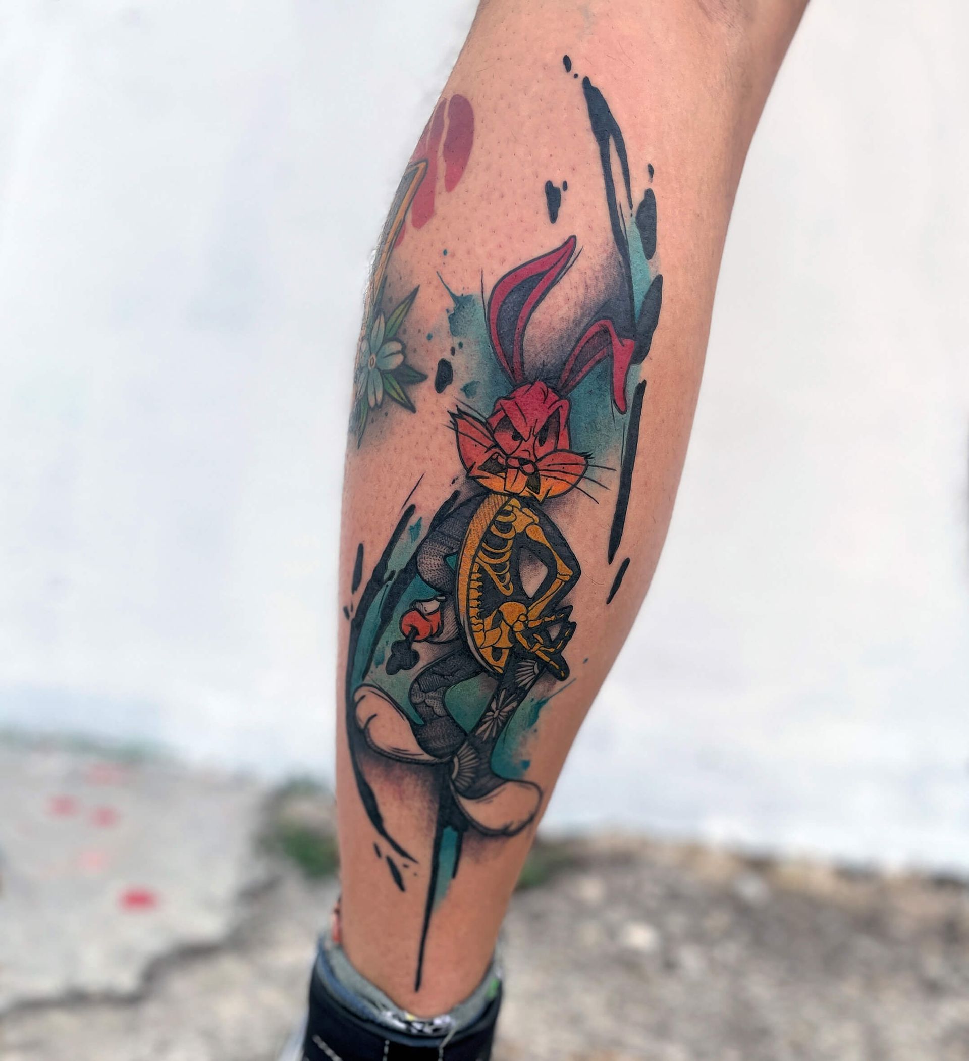 Tätowierung eines Häschens mit Skelettkörper und einem bunten Aquarellklecks auf einem Bein.