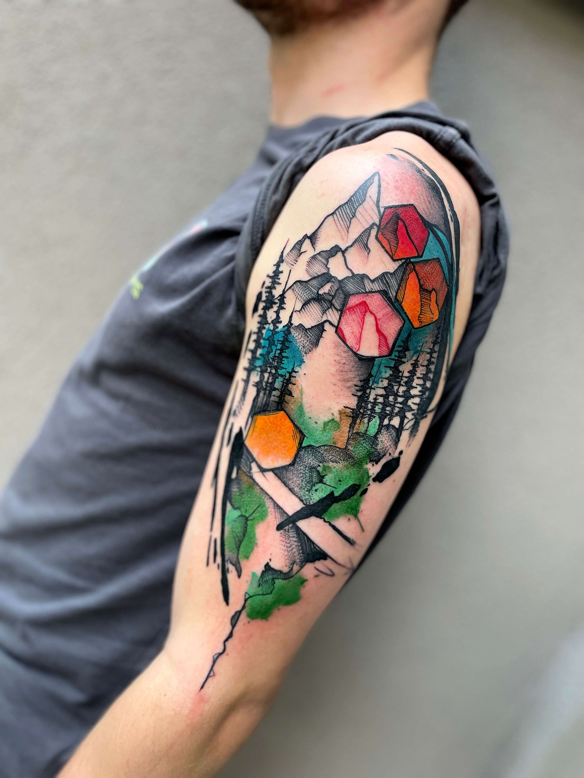 Tätowierung einer Berglandschaft mit bunten geometrischen Formen auf dem Oberarm einer Person.