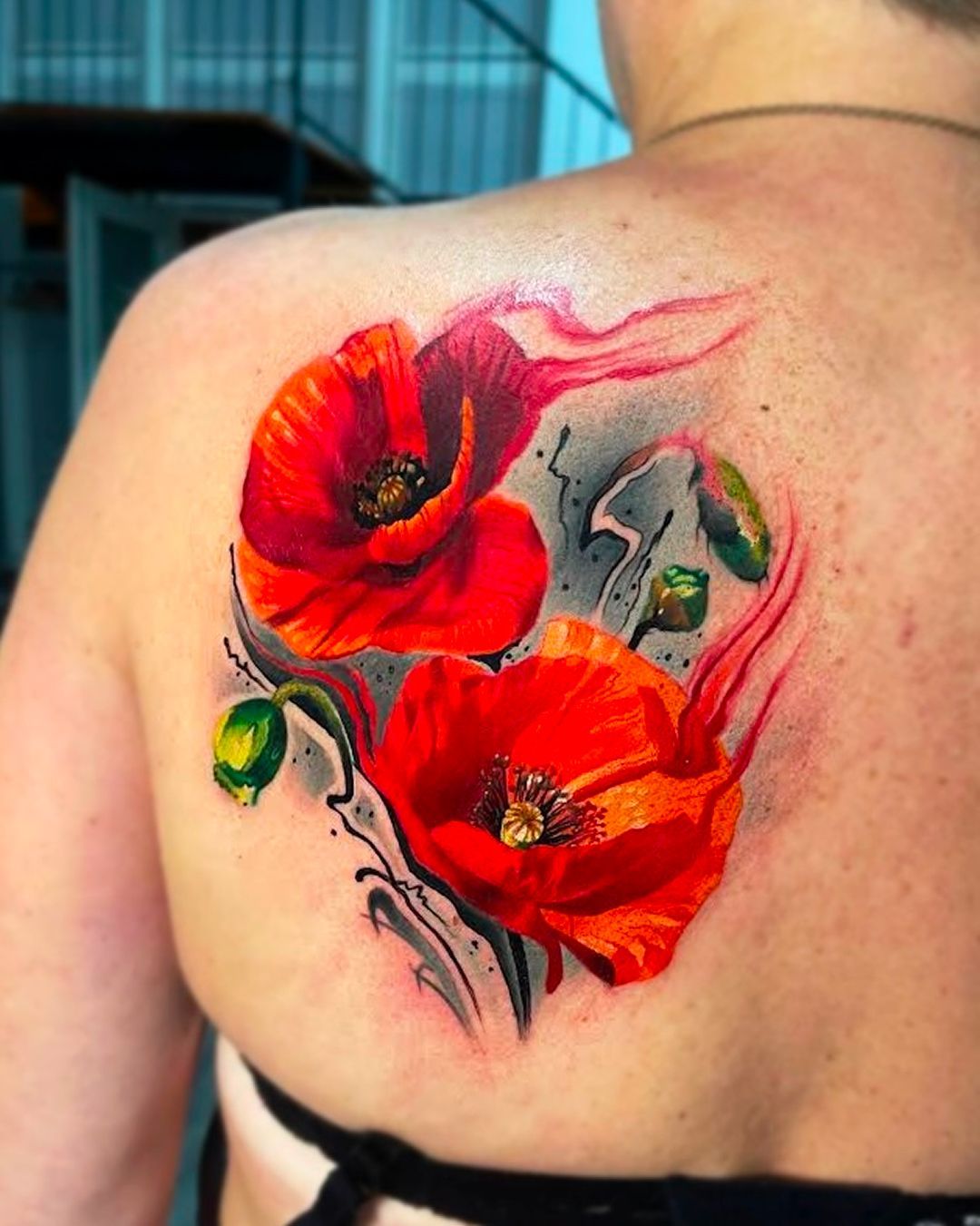 A woman has a tattoo of red flowers on her back.
