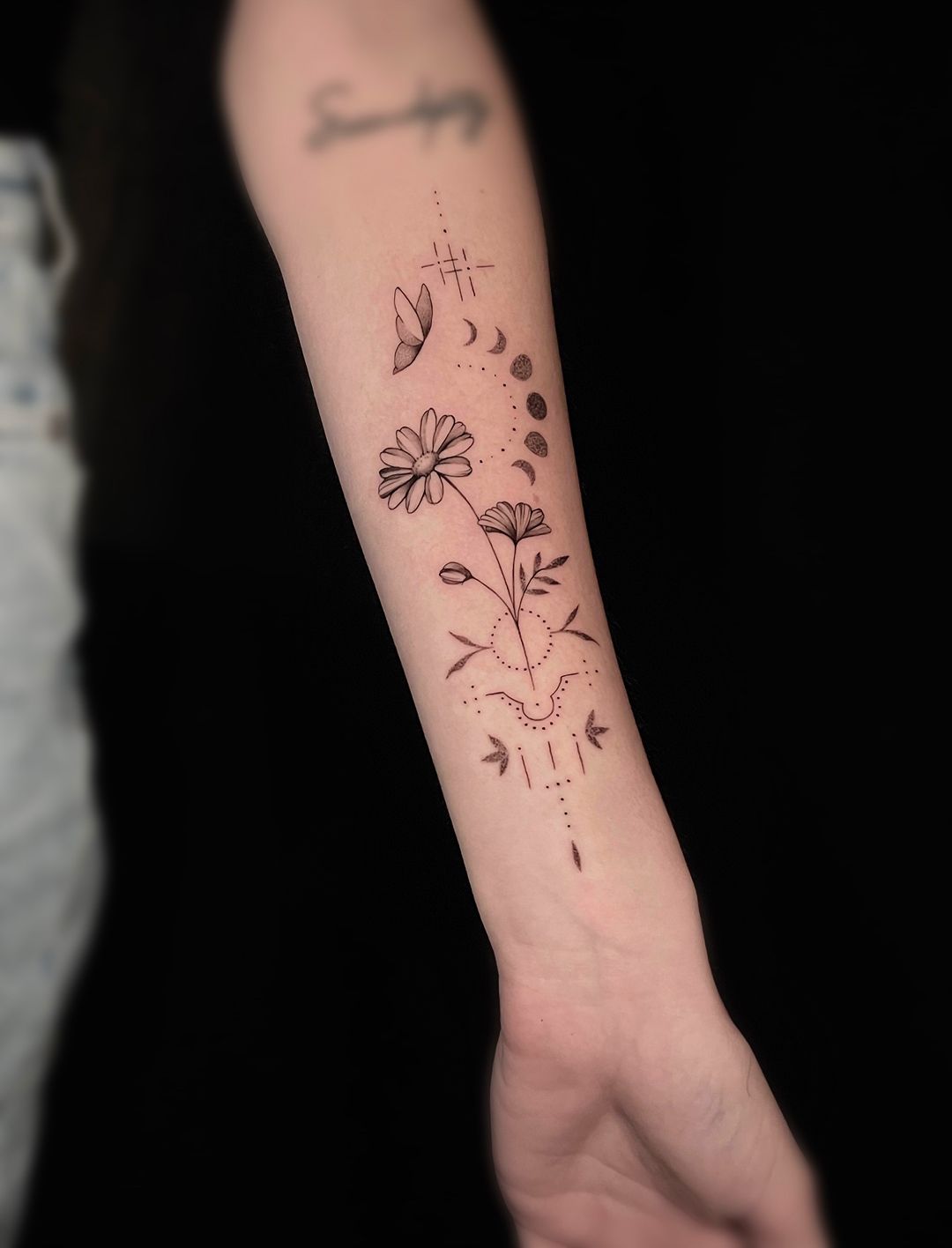 A woman has a tattoo of flowers and leaves on her forearm.