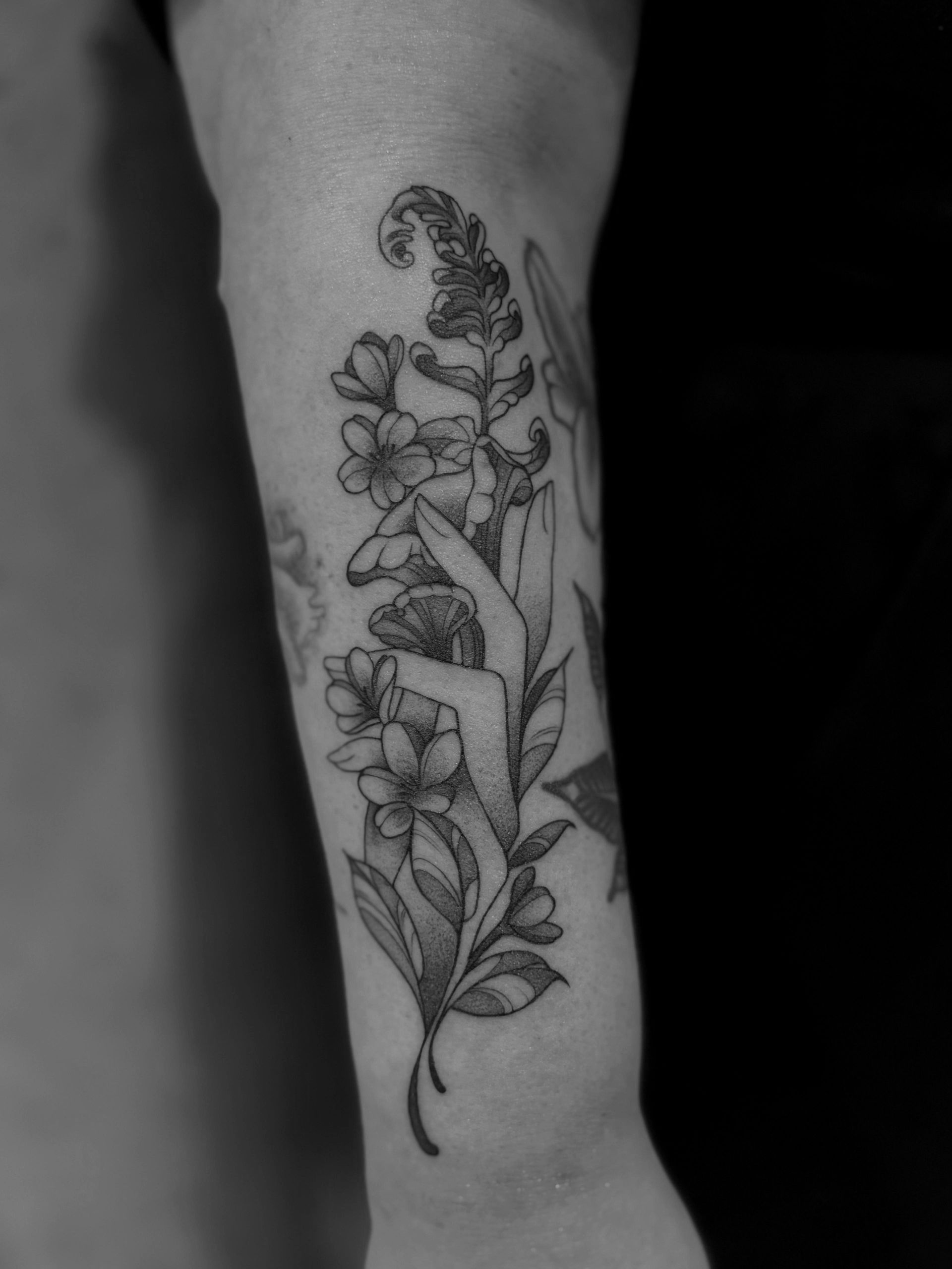 Schwarz-weißes Blumentattoo auf dem Arm einer Person, neben einem Button-Down-Hemd.