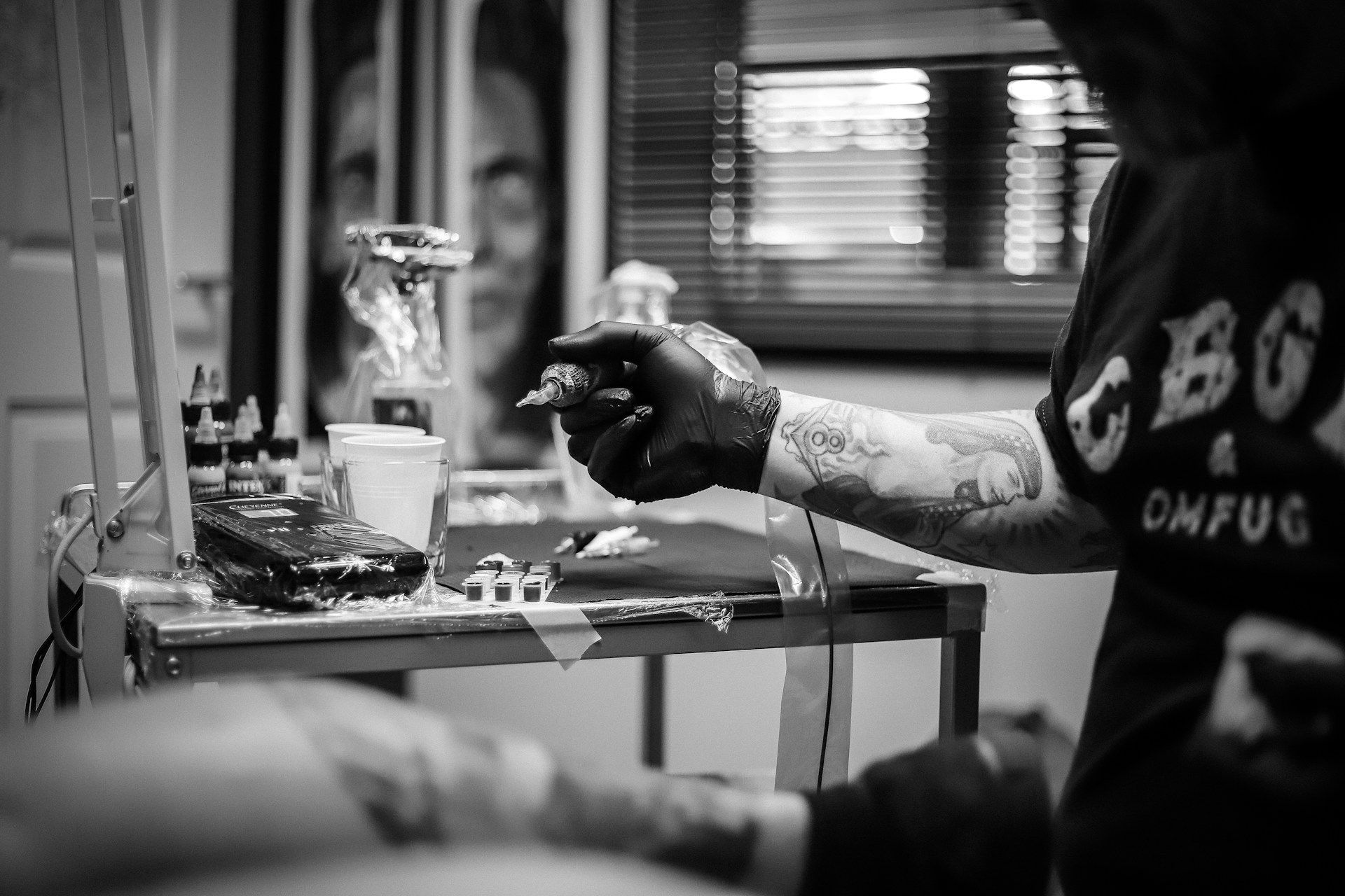 A man is getting a tattoo on his arm in a black and white photo.