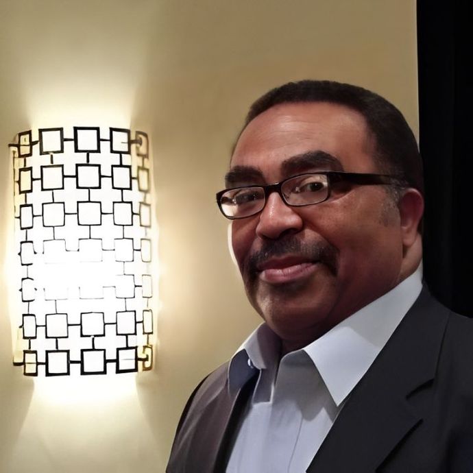 A man wearing glasses stands in front of a wall light