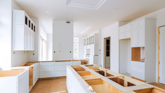 A kitchen under construction with white cabinets and wooden counter tops.