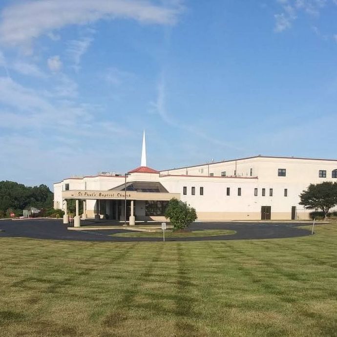 A large white building with a steeple is surrounded by a lush green field.