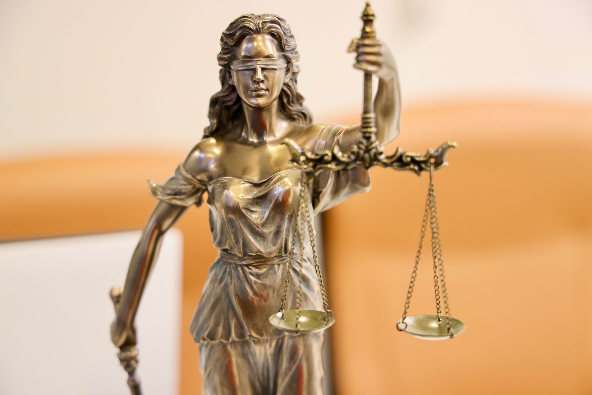 Bronze Lady Justice statue holding scales and sword against a warm blurred background