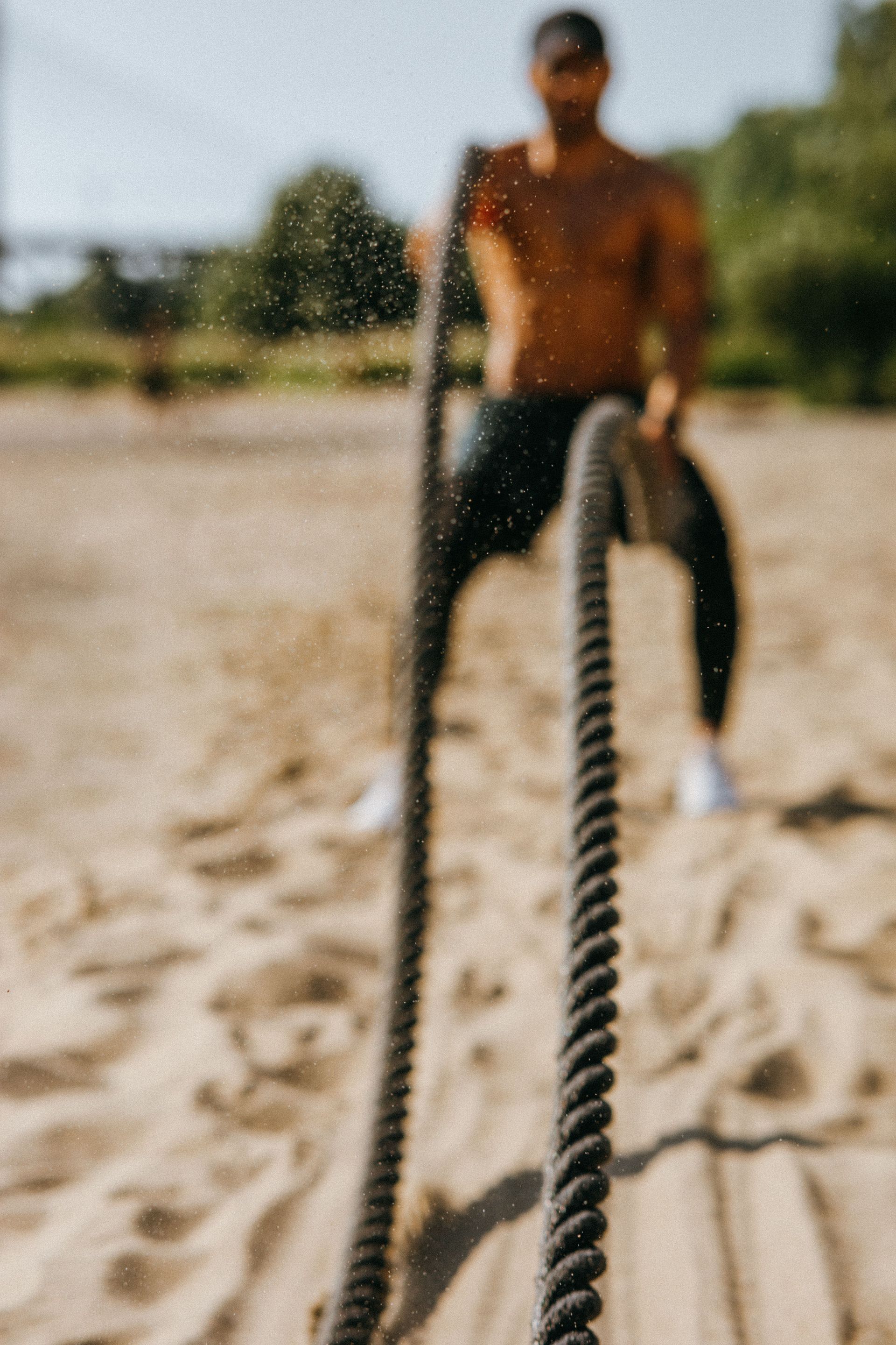 Person pulling a thick rope on a sandy outdoor field, blurred in the background