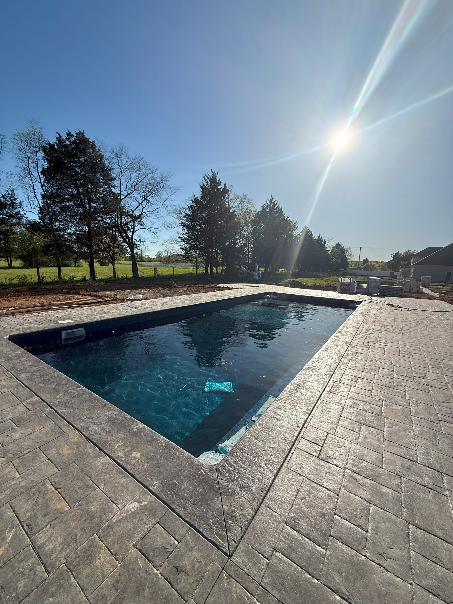 A large swimming pool is surrounded by bricks and trees on a sunny day.