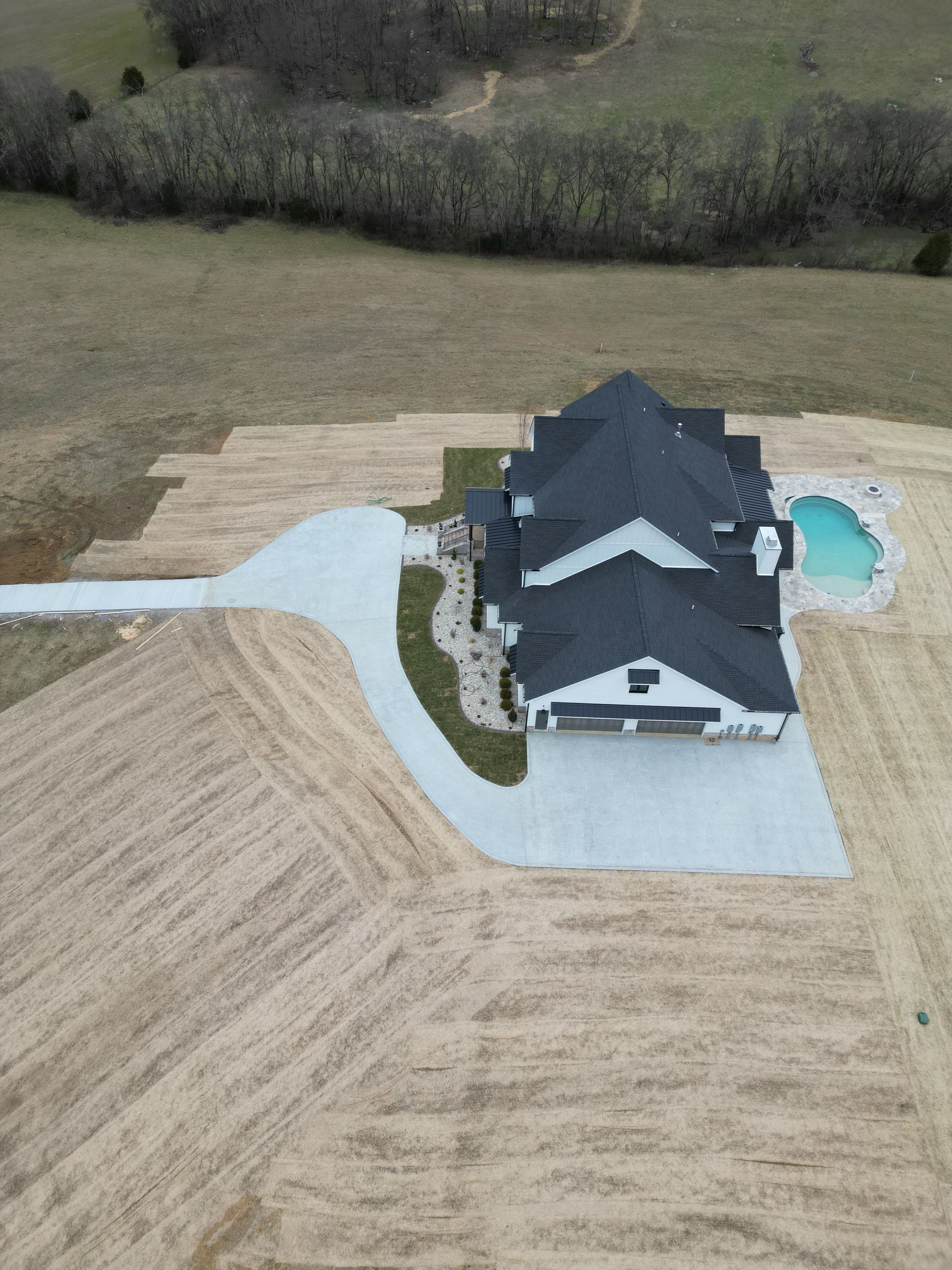An aerial view of a house with a pool in the middle of a field.