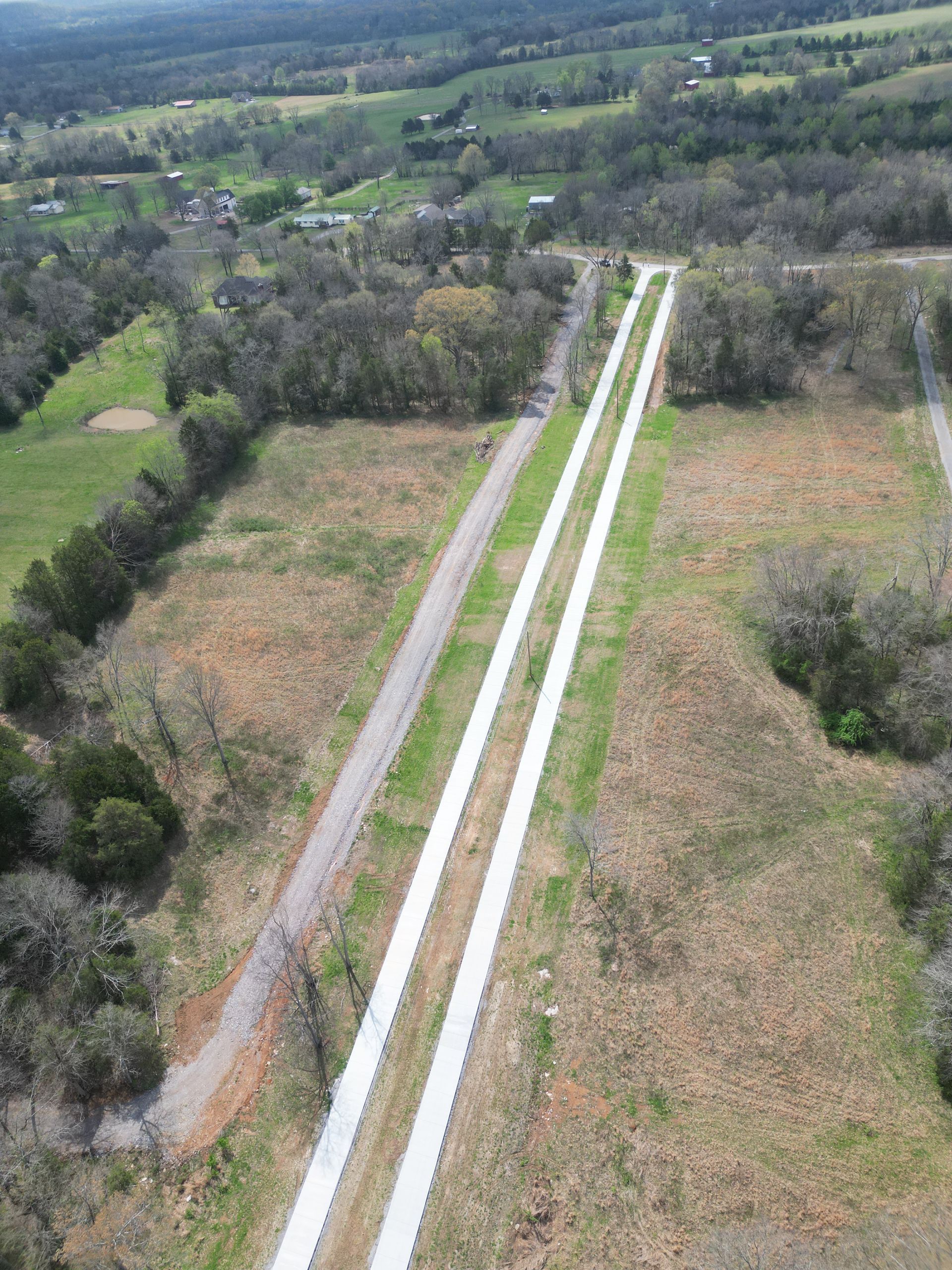 An aerial view of a road going through a lush green field.