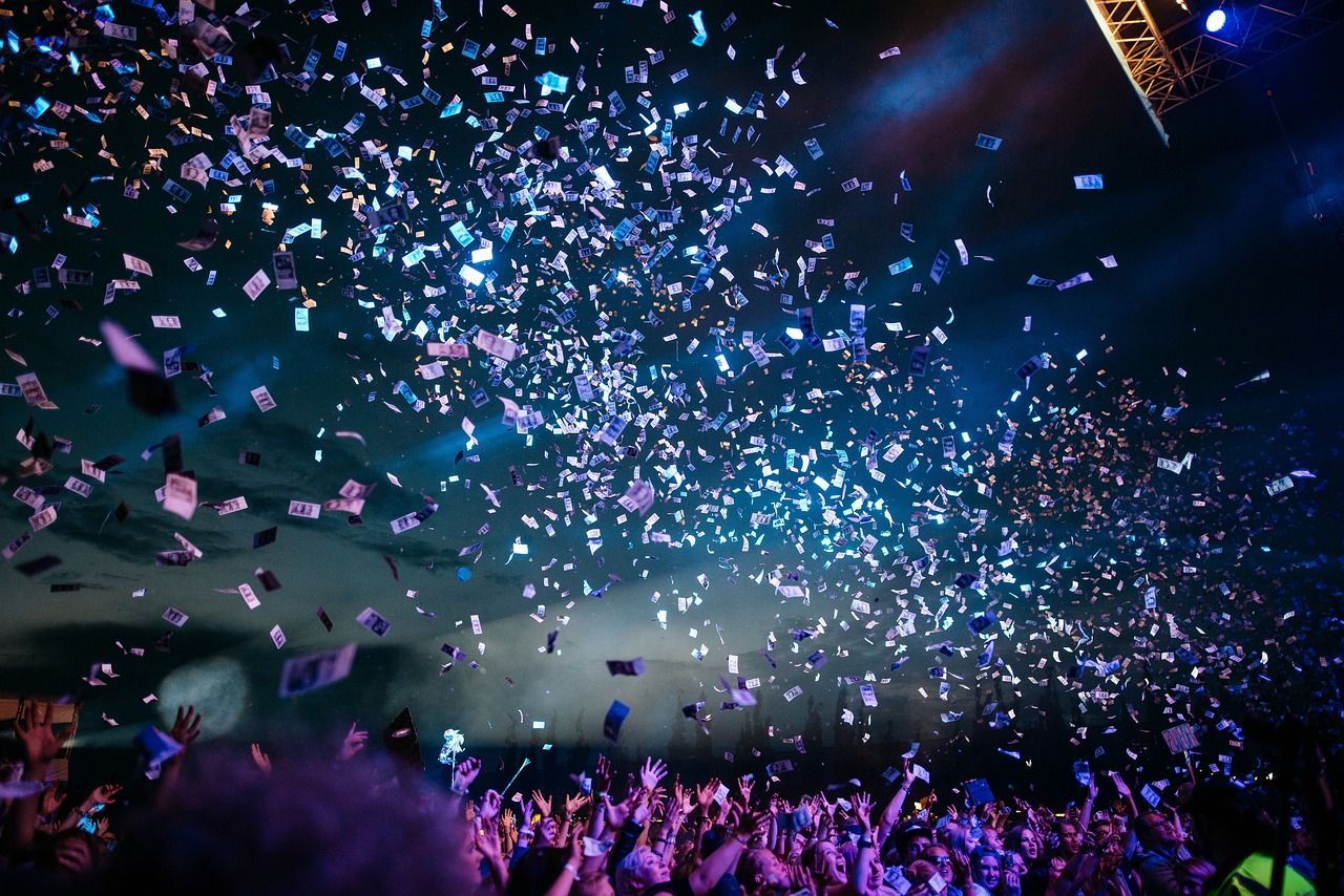 Confetti falling over a cheering crowd at a concert with colorful stage lights.