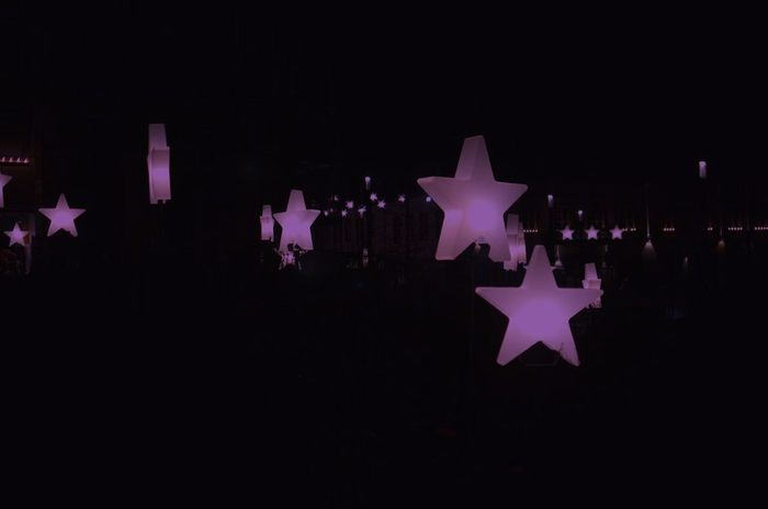 Night scene with multiple illuminated star-shaped lanterns floating above a darkened area, creating a serene and festive atmosphere.
