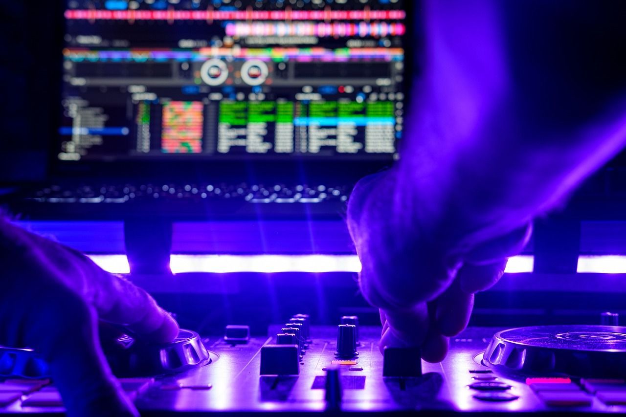 Dj adjusting equipment under purple lighting with a digital audio mixing interface displaying colorful waveforms in the background.