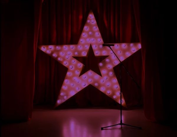 A microphone stand in front of a glowing purple star on a curtain, creating a dramatic and moody stage setting.