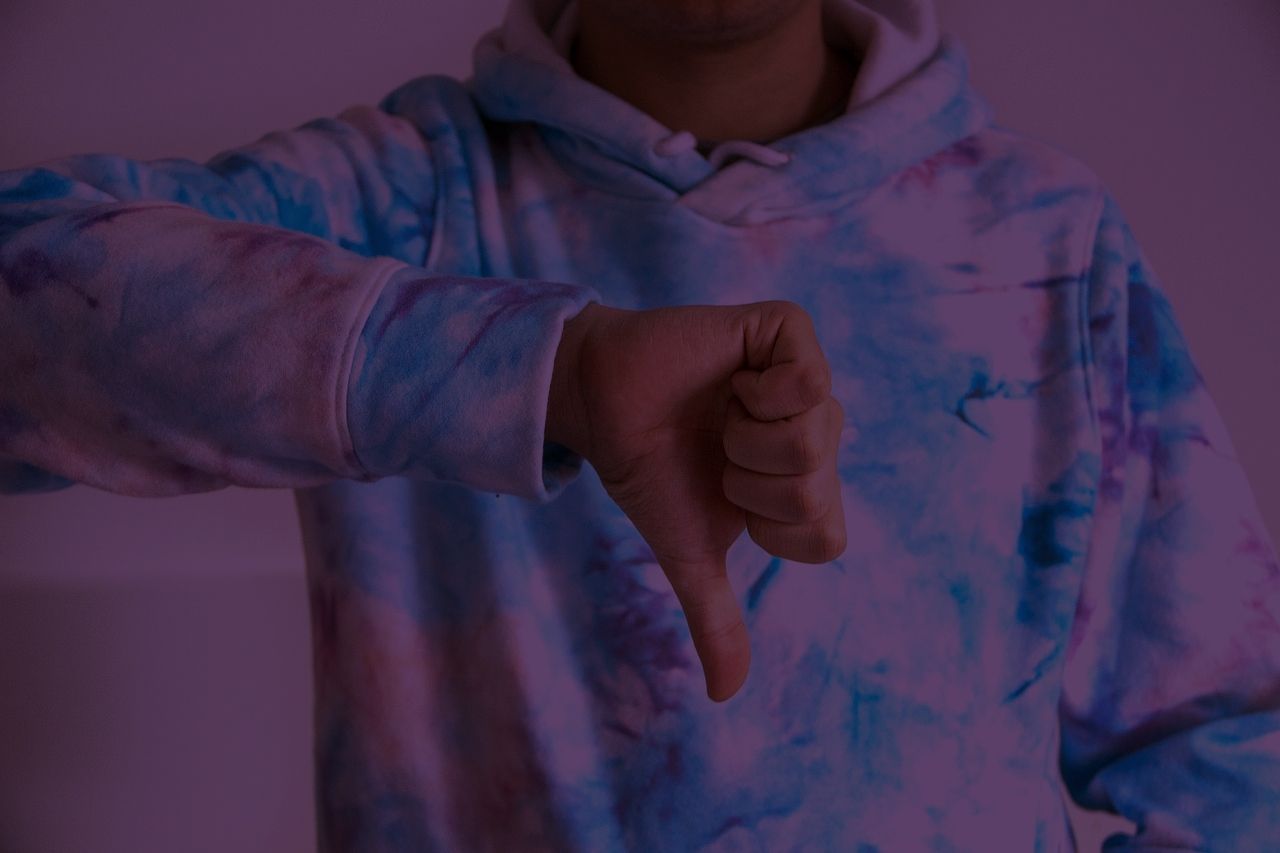 Person in a tie-dye hoodie giving a thumbs-down gesture.