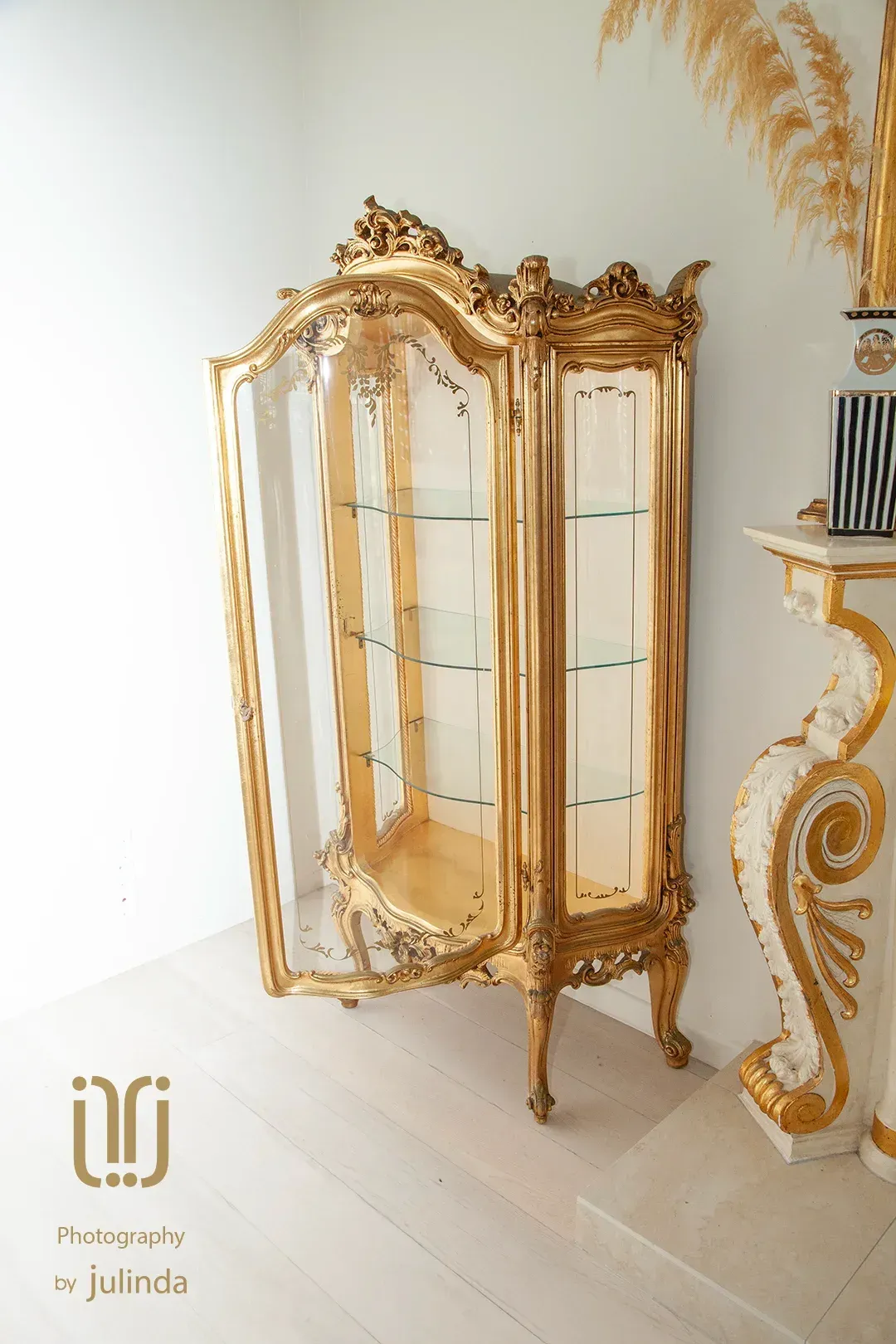 Ornate  24k gold display cabinet in a bright white room, next to a white and gold fireplace. By Julinda at Total Creativeyphotography.