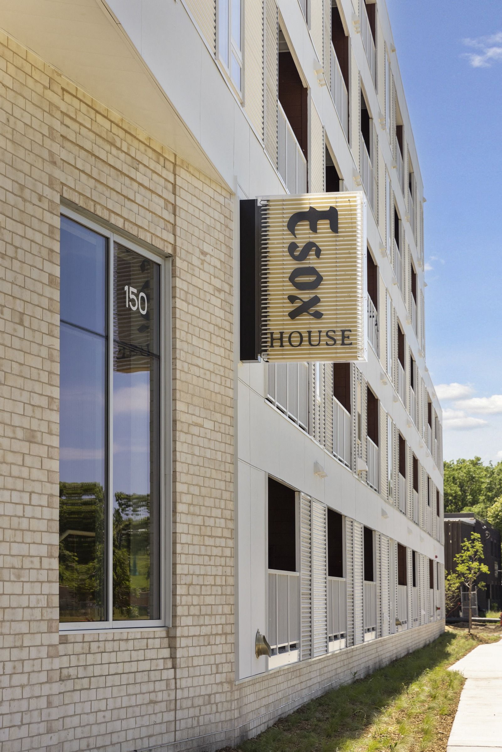 Exterior view of a modern apartment building with a vertical 'ESOX HOUSE' sign on brick wall at Esox House in St. Paul, MN.