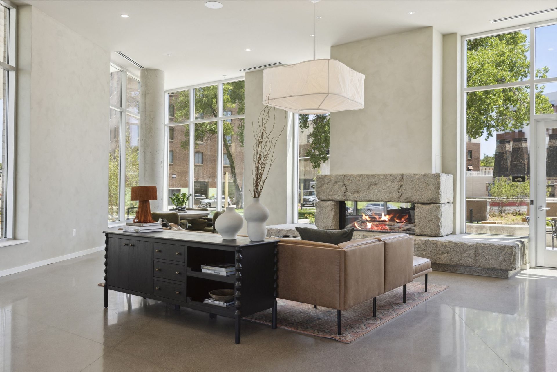 Modern apartment lobby lounge with a leather sofa, stone fireplace, and large windows at Esox House in St. Paul, MN.