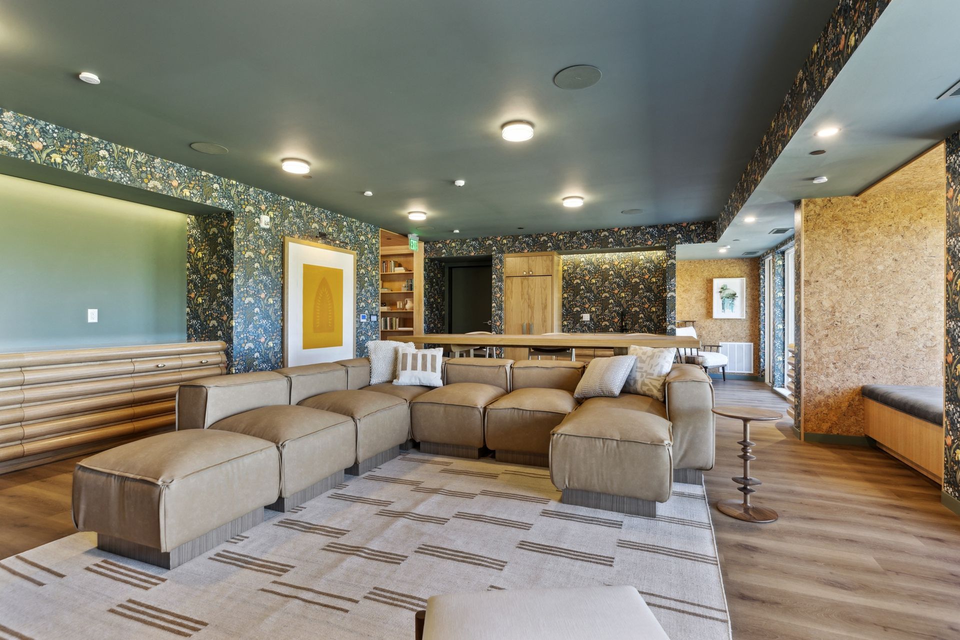 Spacious resident lounge with a tan sectional sofa, patterned wallpaper, and wood accents at Esox House in St. Paul, MN