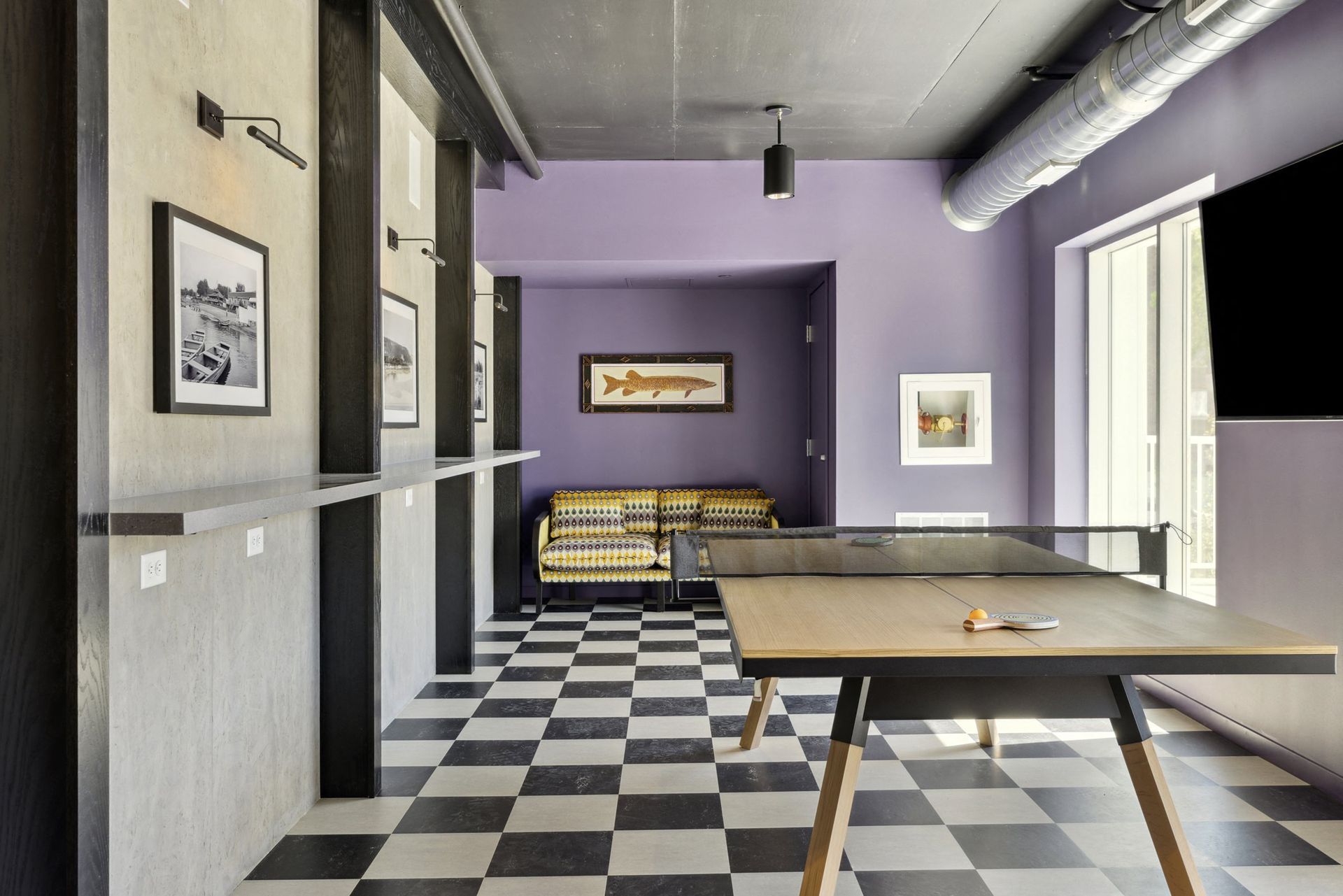 Interior community lounge with checkered floor, purple walls, ping-pong table, and sofa at Esox House in St. Paul, MN.