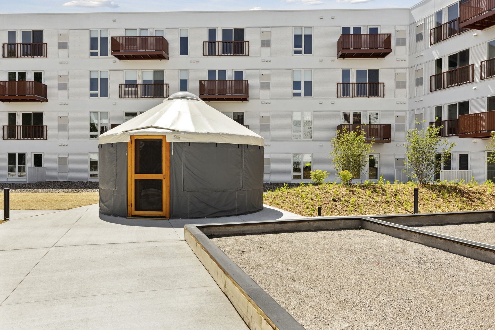 Round tent in a courtyard with an apartment building and balconies behind at Esox House in St. Paul, MN